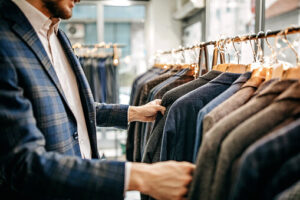 Man dressed in a tweed jacket, looking through a rail of jackets in a shop